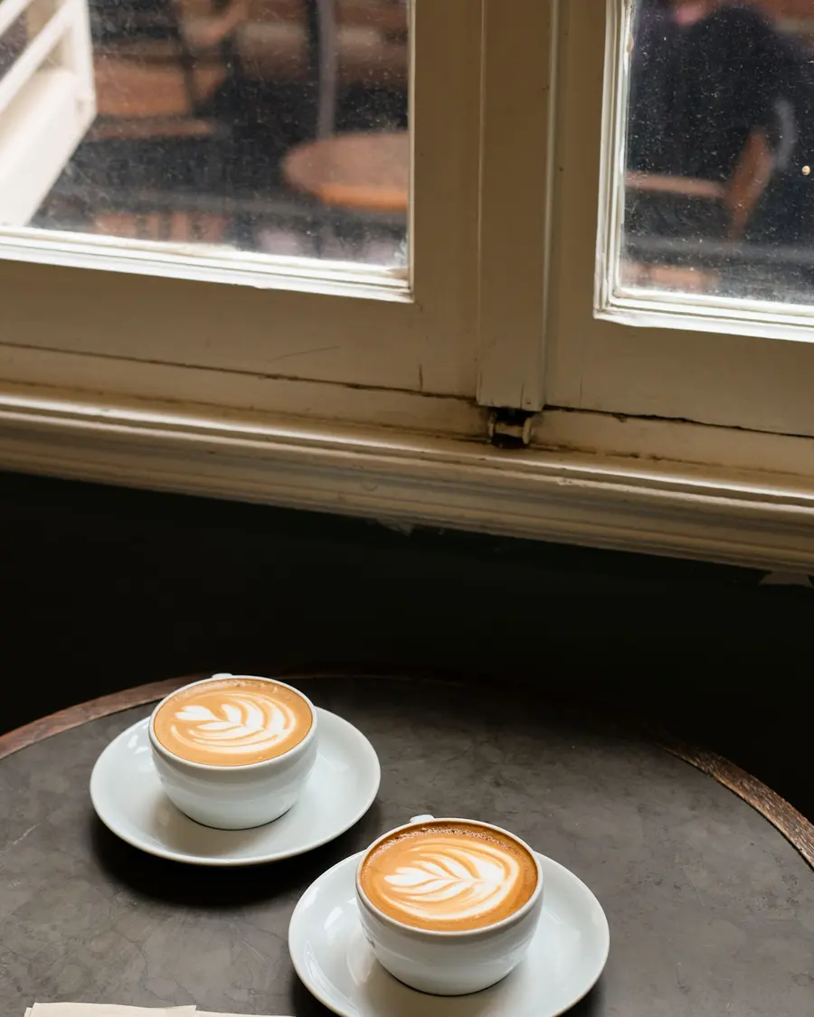 Two cups of latte art coffee on a café table by a window